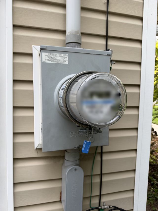 Close view of a GenerLink-equipped smart meter installation with warning label and grounding conductor